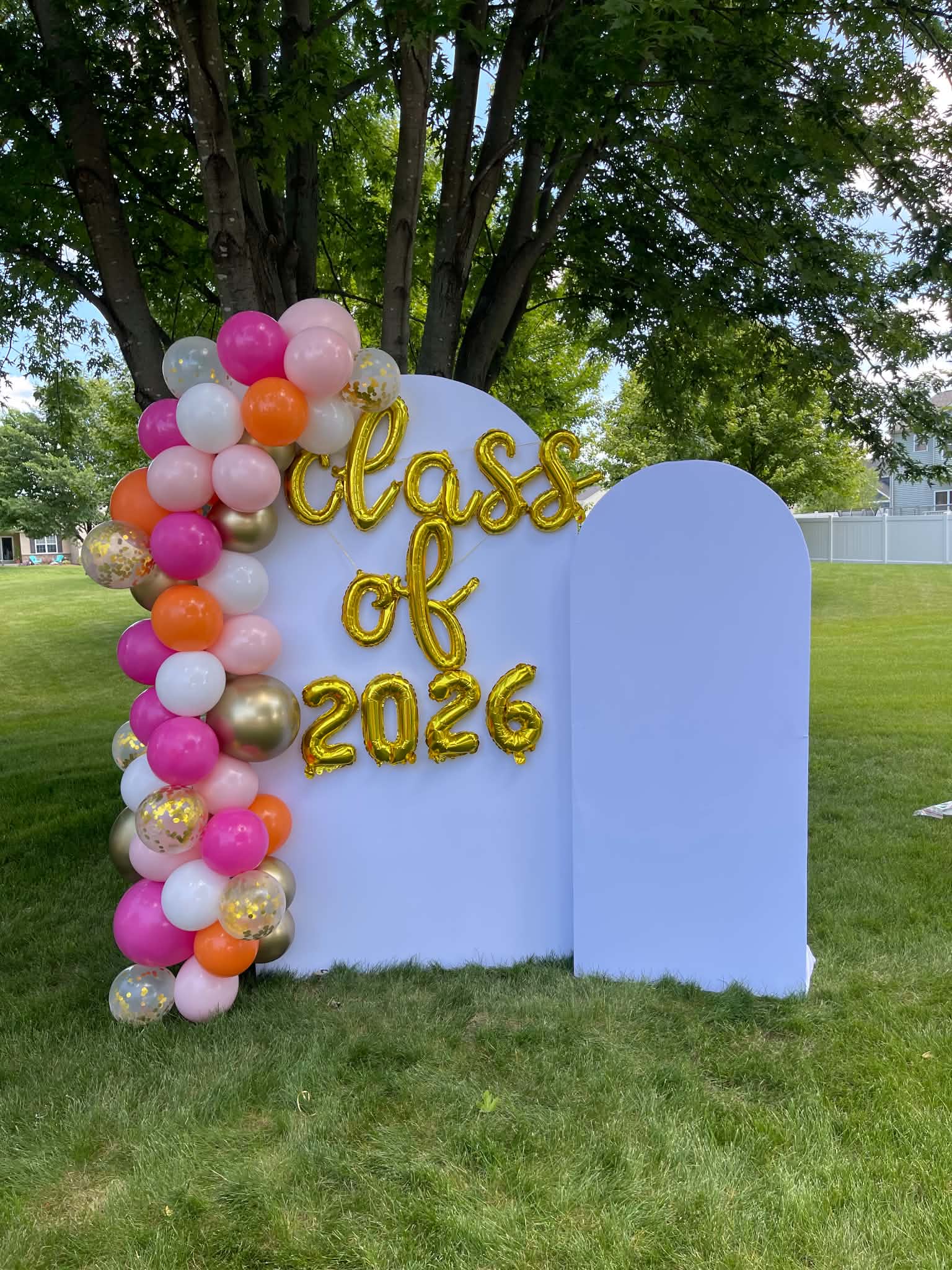 Corrales Designs Aleya Class of 2026 graduation balloon arch with orange, pink, fuchsia, white, and gold balloons